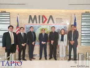 Diplomat taking group photo in front of two Malaysia Flags